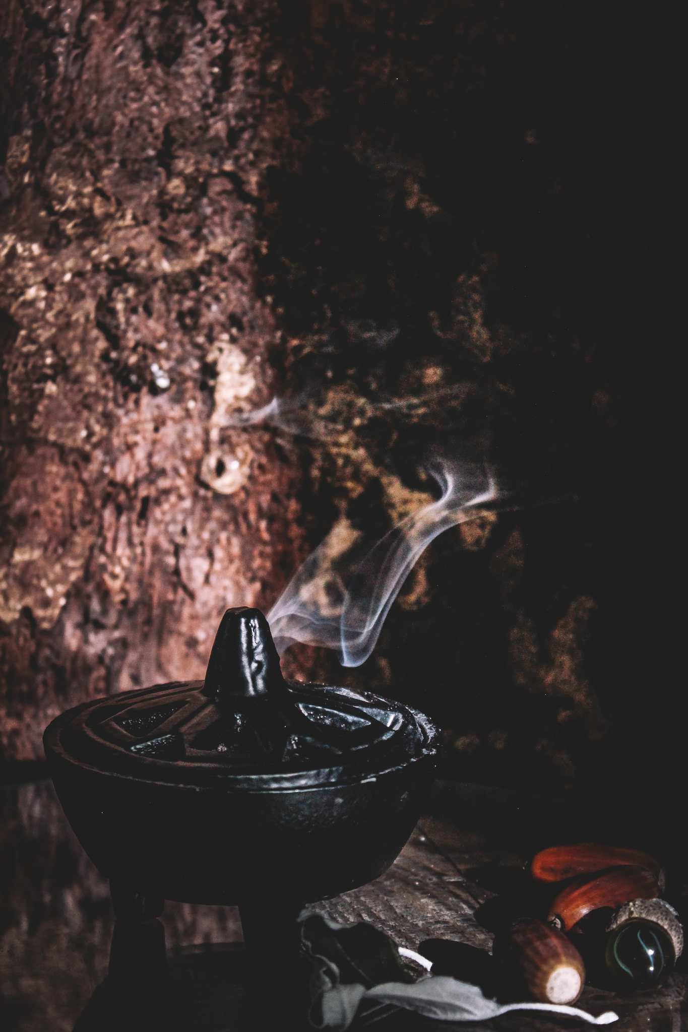Räucherstäbchenhalter, der sanft Rauch freisetzt, vor dem Hintergrund einer rustikalen Holzoberfläche, umgeben von Eicheln und einer kleinen Flasche.