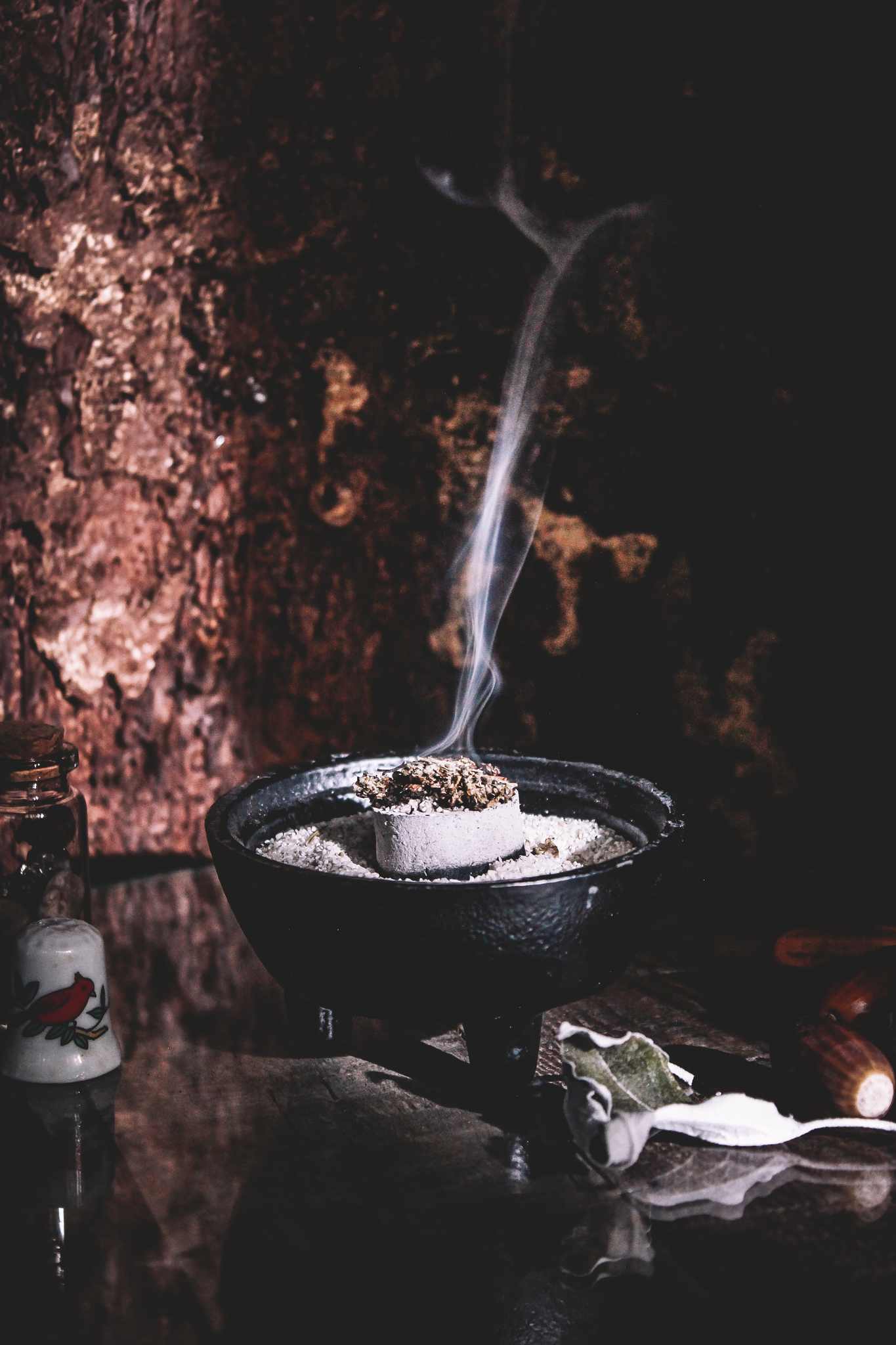 Räucherschale mit aufsteigendem Rauch vor einem rustikalen Hintergrund, brennende Kräuter erzeugen eine mystische und beruhigende Atmosphäre. 