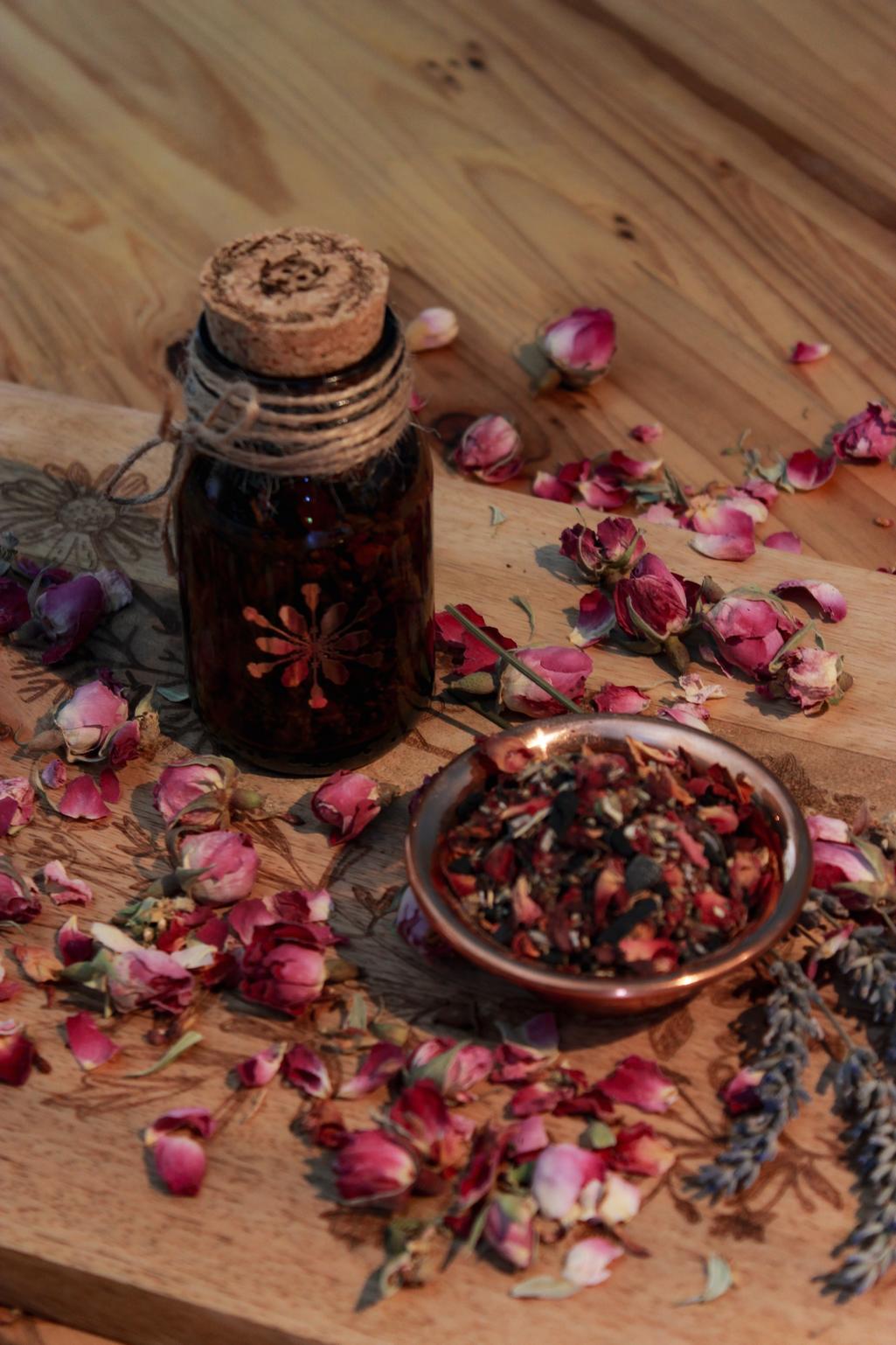 Eine Braunglas-Flasche mit Korken, der mit einem Marienkäfer versehen ist, steht auf einem Holztisch. Drumherum sind Lavendel- und Rosenblüten. Das kupferfarbene Etikett zeigt das Hollenkraut-Logo. Neben dem Glas steht eine kleine Schale aus Kupfer in der die Räuchermischung zu sehen ist.