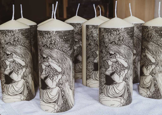 Viele große helle Stumpenkerzen nebeneinander mit einem schwarzen Druck darauf der Frau Holle zeigt, die sich über eine Frau lehnt und an ihre Wange fasst.