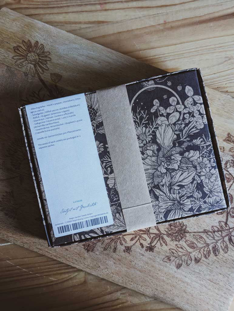 Saatgut Geschenkset in einer schön illustrierten Pappverpackung mit Kräutern und Insekten. Darauf steht: Magic Garden Seeds Samenset Wichtige Heilpflanzen der Frauenheilkunde - Rückseite