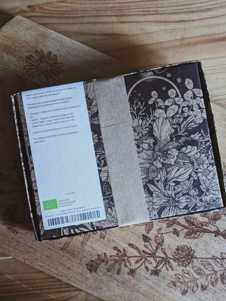 Saatgut Geschenkset in einer schön illustrierten Pappverpackung mit Kräutern und Insekten. Darauf steht: Magic Garden Seeds Samenset Aromatische Kräuter für das rituelle Räuchern - Rückseite