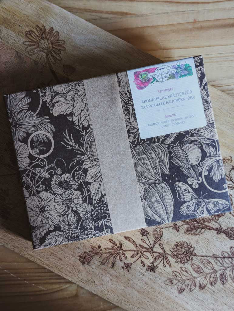 Saatgut Geschenkset in einer schön illustrierten Pappverpackung mit Kräutern und Insekten. Darauf steht: Magic Garden Seeds Samenset Aromatische Kräuter für das rituelle Räuchern