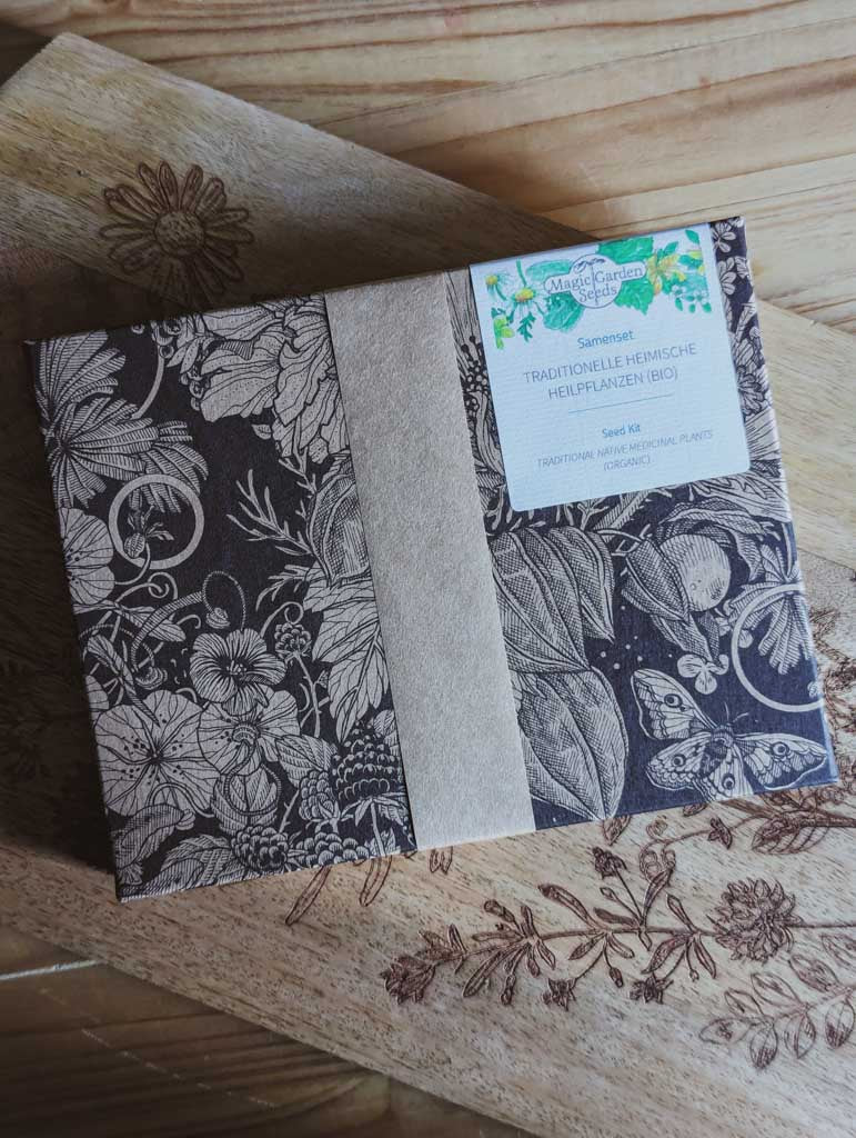 Saatgut Geschenkset in einer schön illustrierten Pappverpackung mit Kräutern und Insekten. Darauf steht: Magic Garden Seeds Samenset Traditionelle heimische Heilpflanzen