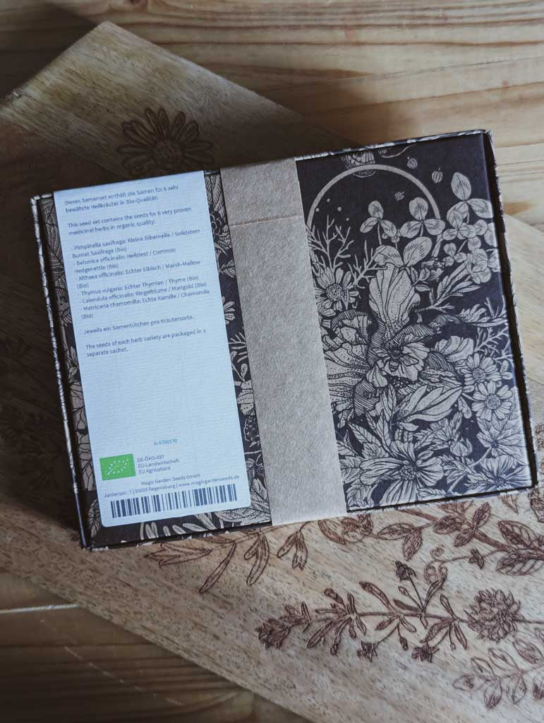 Saatgut Geschenkset in einer schön illustrierten Pappverpackung mit Kräutern und Insekten. Darauf steht: Magic Garden Seeds Samenset Traditionelle heimische Heilpflanzen - Rückseite