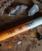 Eine Stabkerze liegt auf einem Holzbrett. Drumherum Steine und Halloween-Streudeko. Die Kerze ist gelb orange und weiß. Auf ihr steht in schwarzer Schrift: Trick or Treat