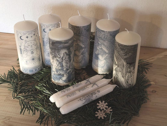 Mehrere weiße Kerzen mit verschiedenen Motiven stehen oder liegen auf Tannenzweigen.