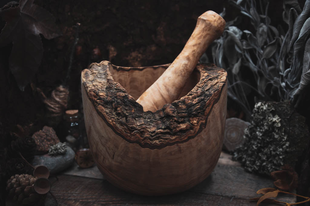 Rustikales, handgefertigtes Mörser- und Stößelset aus natürlichem Holz, umgeben von getrockneten Kräutern und Pflanzen, perfekt für das Zermahlen von frischen Kräutern, Gewürzen und anderen Zutaten.