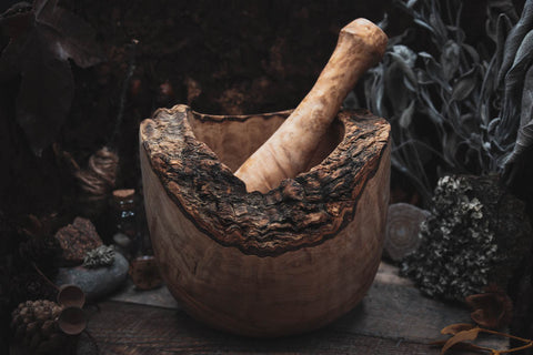 Rustikales, handgefertigtes Mörser- und Stößelset aus natürlichem Holz, umgeben von getrockneten Kräutern und Pflanzen, perfekt für das Zermahlen von frischen Kräutern, Gewürzen und anderen Zutaten.