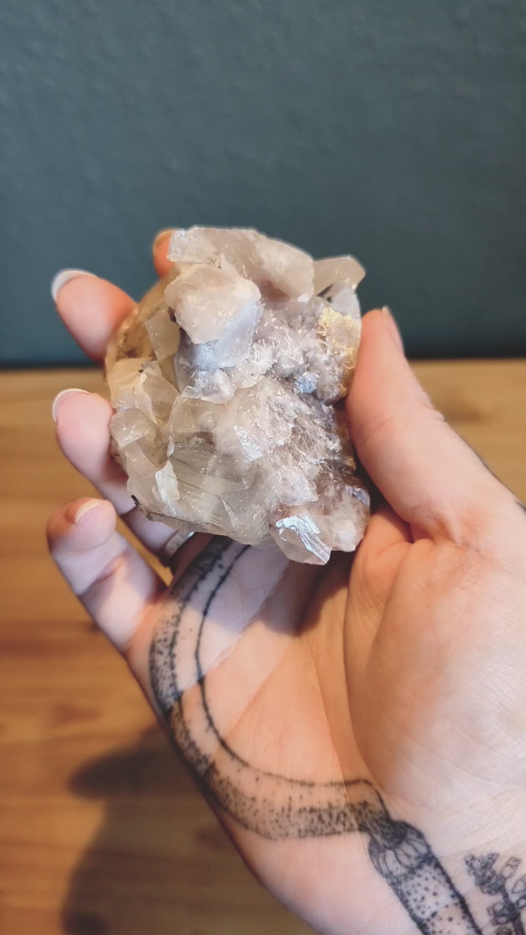 Das Video zeigt ein Stück Calcit, das in einer Hand gehalten wird. Der Calcit hat eine weiße bis leicht rosa Farbe und besteht aus mehreren kristallinen Strukturen, die in verschiedene Richtungen zeigen. Die Oberfläche des Calcits ist teilweise durchsichtig und weist einige Bruchstellen auf, die die kristalline Struktur des Minerals sichtbar machen.