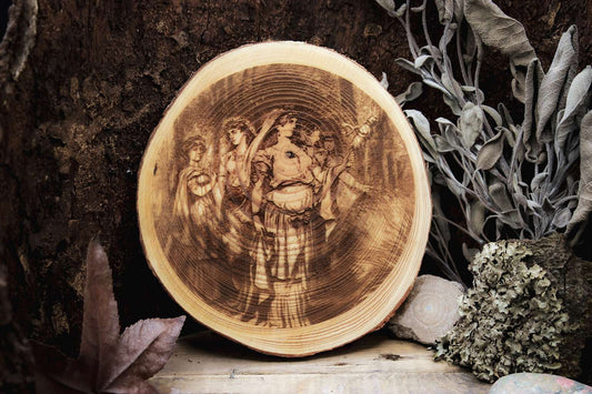 Eine Holzscheibe in die das Bild der Frigg als Ostara eingebrannt ist. Sie wird von mehreren Frauen begleitet.