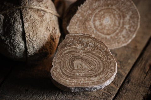 Eichenberger Kugel, Aragonit-Paar aus Österreich - Das Bild zeigt mehrere runde Aragoniten und zwei geschnittene Aragoniten auf einer gealterten Holzoberfläche. Der Aragonit hat eine raue Textur und ist braun. Die anderen Aragoniten zeigen deutliche Ringe und haben eine texturierte Oberfläche. Die Schnur, die den Aragonit bindet, ist dünn und wirkt rustikal. Die gealterte Holzoberfläche unter diesen Objekten hat sichtbare Körner und Texturen. Die gesamte Stimmung des Bildes ist rustikal und natürlich.