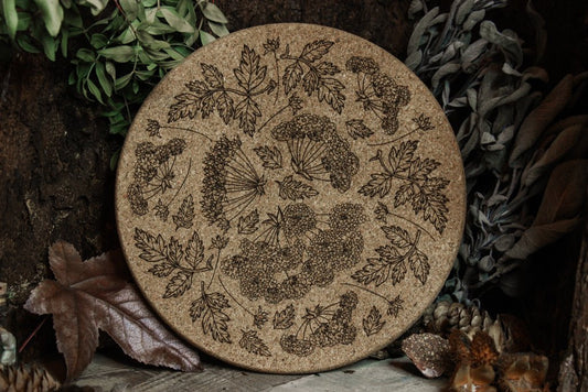 Großer Untersetzer aus Kork "Kräuter" - Dekoratives, rundes Kork-Tablett mit detaillierten Gravuren von Blumen, präsentiert auf einem dunklen Hintergrund mit grünen Blättern