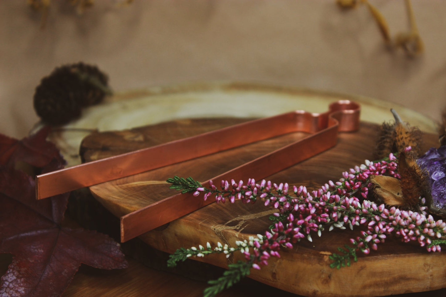 Räucherset: Zange, Schale, Löffel, Räucherkohle und Sand - Elegante Kupferzange auf einem rustikalen Holzbrett, umgeben von herbstlichen Blättern und Blumen. 
