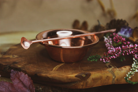 Räucherset: Zange, Schale, Löffel, Räucherkohle und Sand - Eleganter Kupferlöffel auf einem rustikalen Holzbrett, umgeben von herbstlichen Blättern und Blumen. 