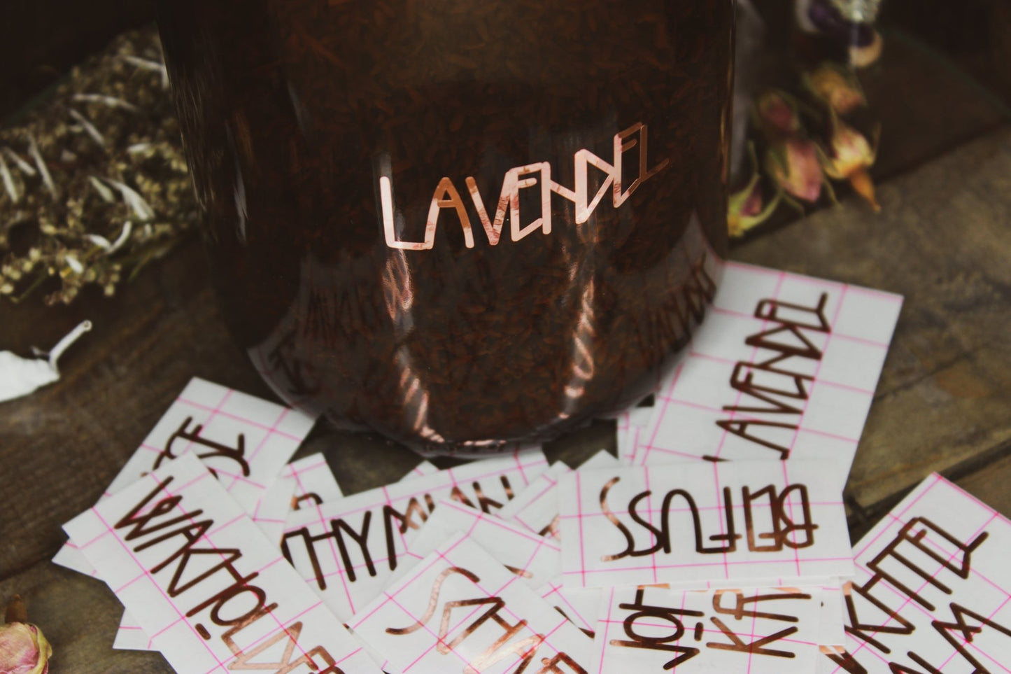 Vinyl Sticker Set "Heilkräuter" -Dunkelbrauner Behälter mit der Aufschrift ‘LAVENDEL’, umgeben von Stickern und getrockneten Blumen auf einem rustikalen Holzhintergrund. 