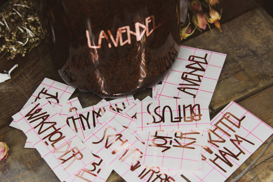 Vinyl Sticker Set "Heilkräuter" -Dunkelbrauner Behälter mit der Aufschrift ‘LAVENDEL’, umgeben von Stickern und getrockneten Blumen auf einem rustikalen Holzhintergrund. 