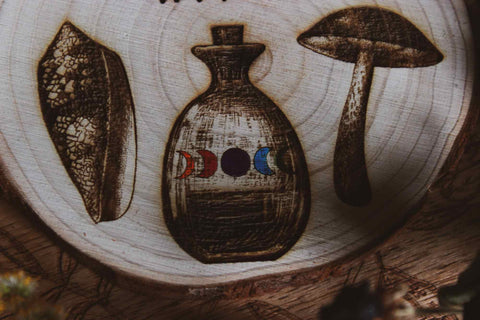 Nahaufnahme Wandbild aus Holz "Autistic Witch" - Handgefertigte Holzgravur  detailliertee Zeichnungen eines Blattes, einer Flasche mit farbiger Flüssigkeit und eines Pilzes. 