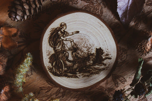 Wandbild aus Holz "Freyja im Katzenwagen" - Wandbild aus Holz "Freyja im Katzenwagen" - “Handgefertigtes Kunstwerk auf einem kreisförmigen Holzstück, das eine Freya auf einem Zugwagen darstellt, Katzen ziehen ihn Das Kunstwerk ist umgeben von Naturmaterialien wie Tannenzapfen und Blättern. 