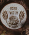 Wandbild aus Holz "Herb Witch" - Wandbild aus Holz "Herb Witch" - Dieses Bild zeigt eine kunstvoll gravierte Holzscheibe mit der Inschrift “HERB WITCH”, umgeben von einer natürlichen und mystischen Atmosphäre. Die Gravur stellt eine Tasse Tee dar, die von zwei Zweigen mit Blättern flankiert wird, 