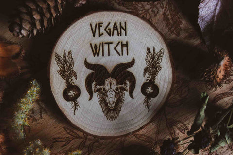 Wandbild aus Holz "Vegan Witch" - Das Bild zeigt ein handgefertigtes Kunstwerk mit der Inschrift “VEGAN WITCH”, umgeben von einer dunklen, mystischen Atmosphäre und natürlichen Elementen wie Tannenzapfen und Blättern.