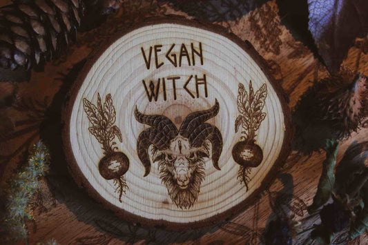 Wandbild aus Holz "Vegan Witch" - Wandbild aus Holz "Vegan Witch" - Das Bild zeigt ein handgefertigtes Kunstwerk mit der Inschrift “VEGAN WITCH”, umgeben von einer dunklen, mystischen Atmosphäre und natürlichen Elementen wie Tannenzapfen und Blättern.