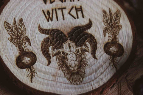 Nahaufnahme Wandbild aus Holz "Vegan Witch" - Das Bild zeigt ein handgefertigtes Kunstwerk mit der Inschrift “VEGAN WITCH”, umgeben von einer dunklen, mystischen Atmosphäre und natürlichen Elementen wie Tannenzapfen und Blättern.